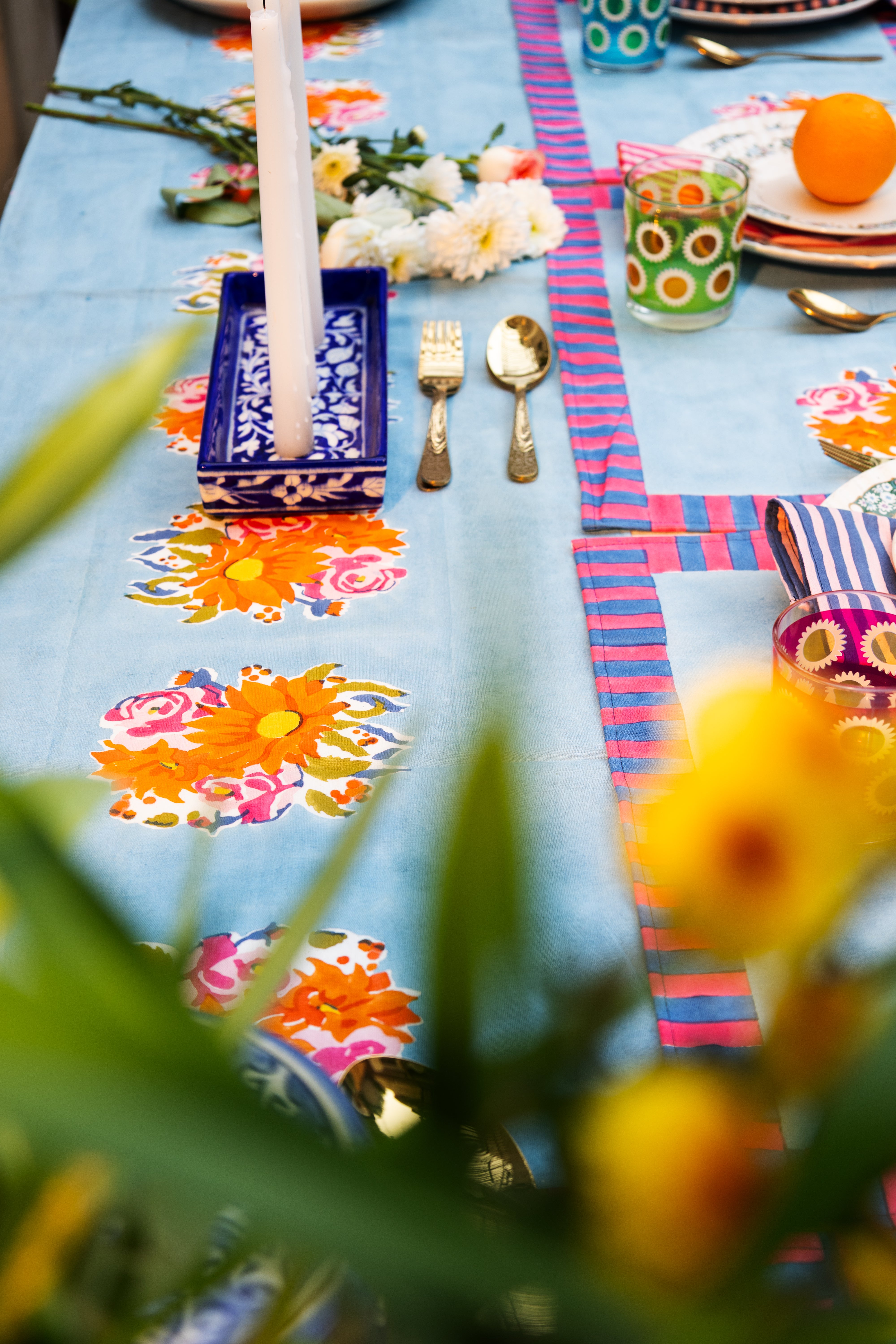 Decorative blue cotton table runner with expressive hand-printed florals and a vibrant striped border, capturing the "freedom of bloom".