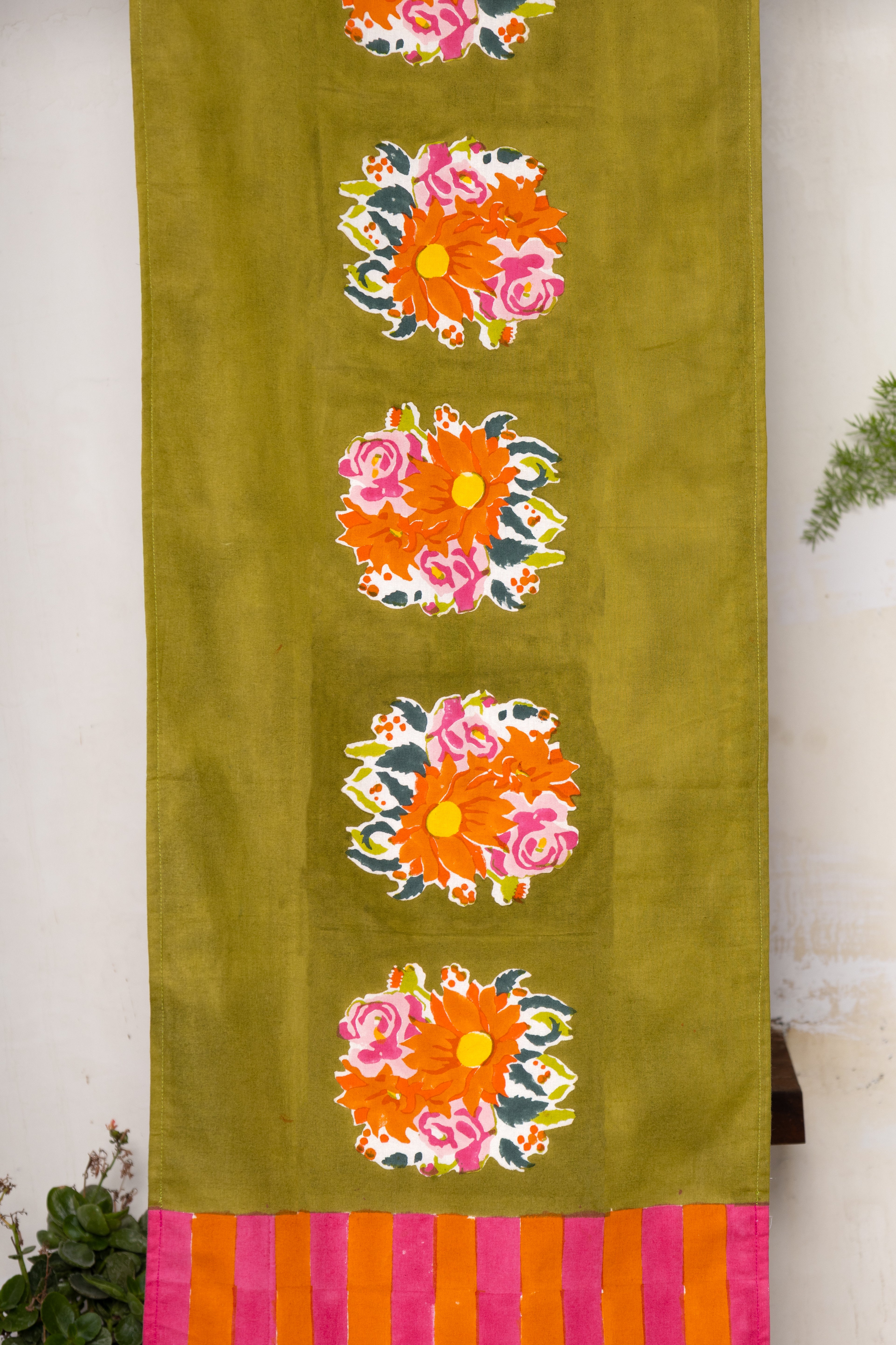 Decorative green cotton table runner with hand-printed floral motifs and a contrasting striped border, capturing the "freedom of bloom" .